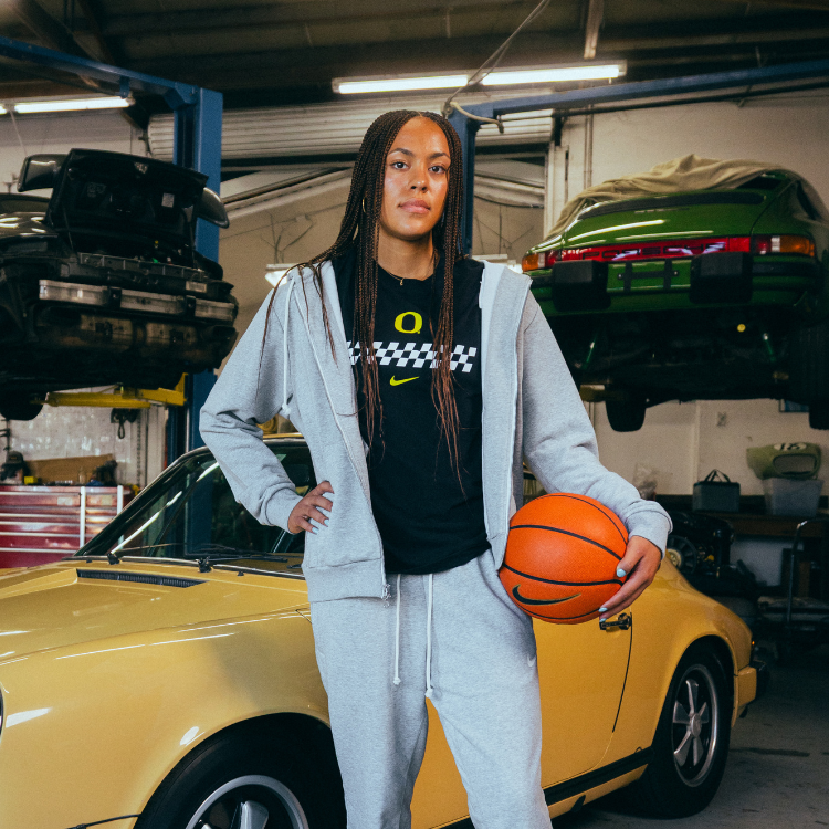Sofia Bell holding a basketball in a garage with cars in the background. She is wearing the DOAF Speedway Hoodie, T-shirt and Pant.