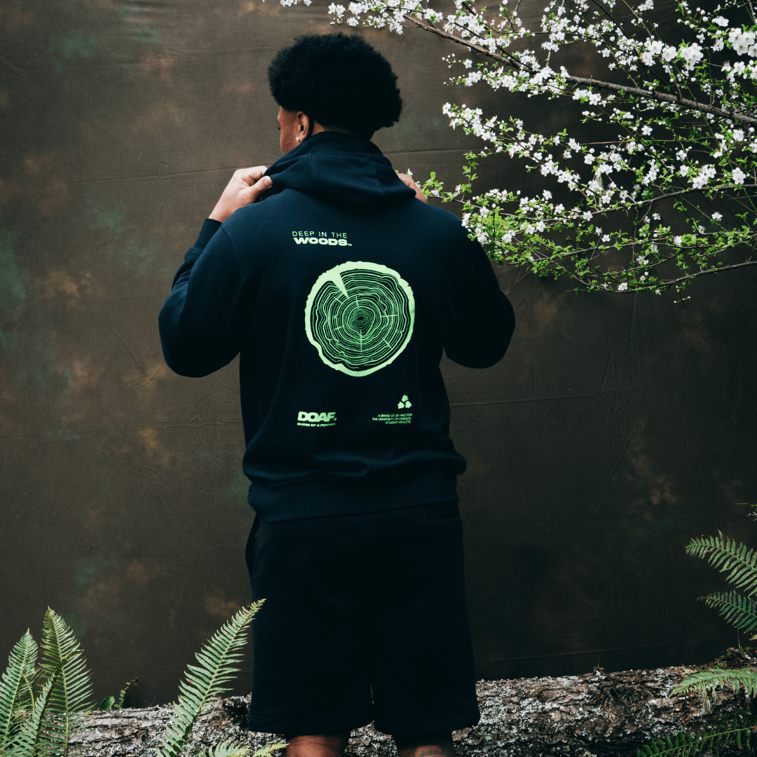 Jerry Mixon wearing a DOAF hoodie with a green logo and text, standing in a natural setting with plants and a tree.