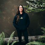 Kiara Romero wearing a black DOAF hoodie with a logo, standing outdoors with greenery around