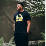 Ziyare Addison wearing a black DOAF t-shirt with a graphic design standing against a natural background with greenery.