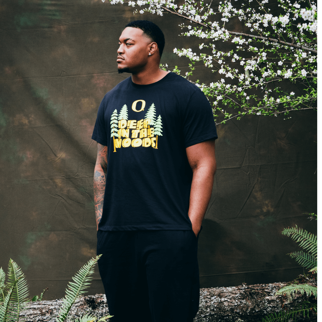 Ziyare Addison wearing a black DOAF t-shirt with a graphic design standing against a natural background with greenery.