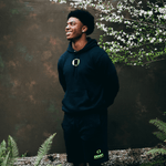 Jerry Mixon wearing a black DOAF hoodie with a logo, standing outdoors with greenery in the background