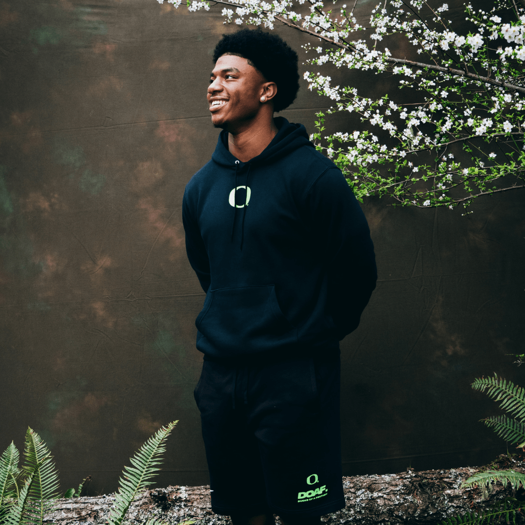 Jerry Mixon wearing a black DOAF hoodie with a logo, standing outdoors with greenery in the background