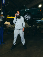 Dante Moore in grey Speedway hoodie and pants holding a football in a garage with a vehicle in the background