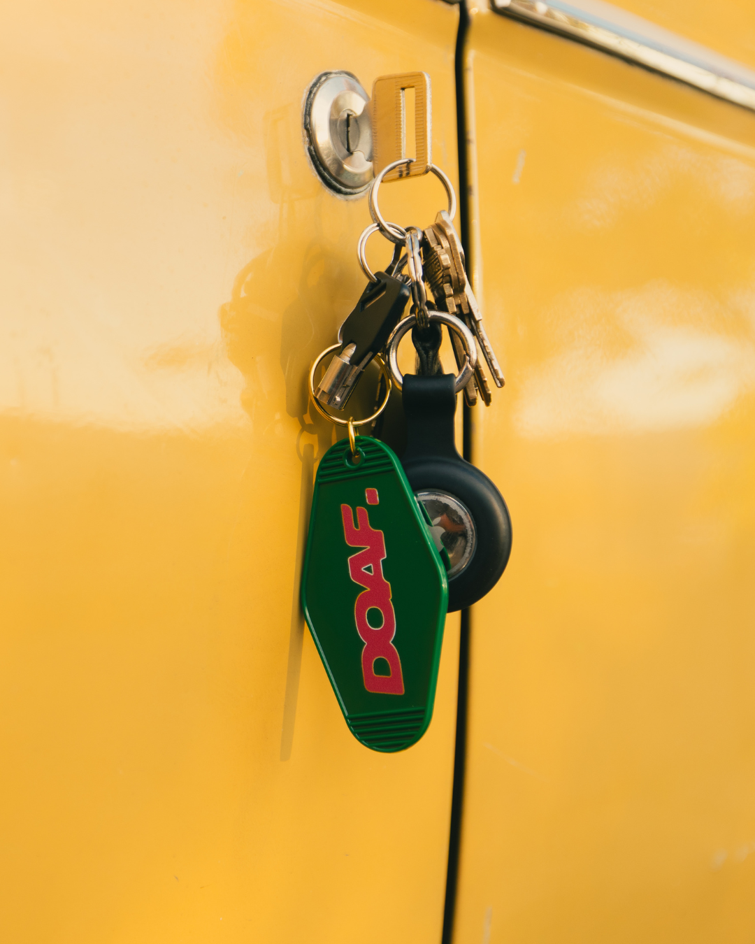 Keychain with DOAF logo attached to a yellow vehicle door handle.