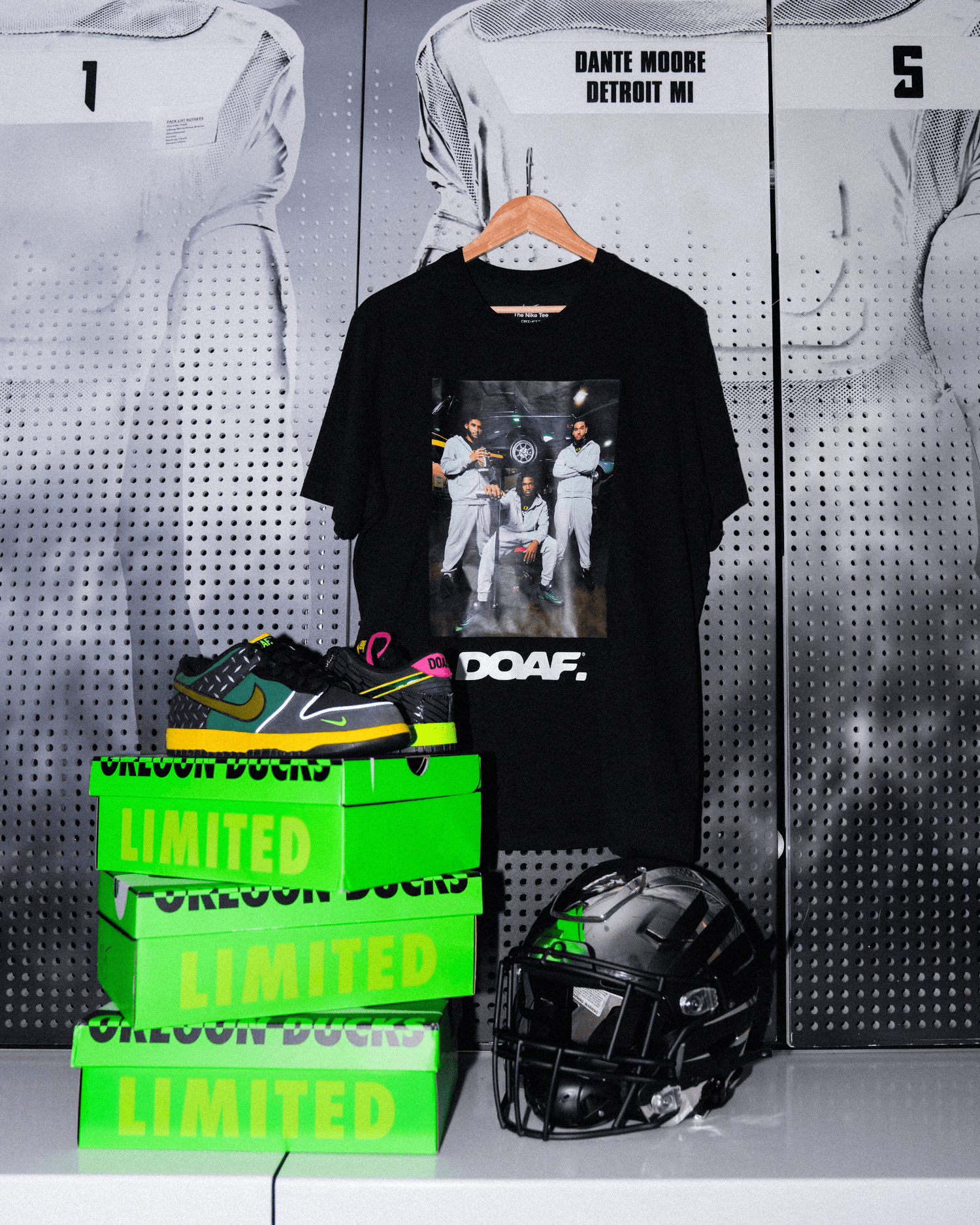 DOAF Tee featuring Dante Moore, Dakorien Moore, and Matayo Uiagalelei hanging up on Dante's locker. There is a football helmet and sneakers stacked on DOAF shoe boxes.