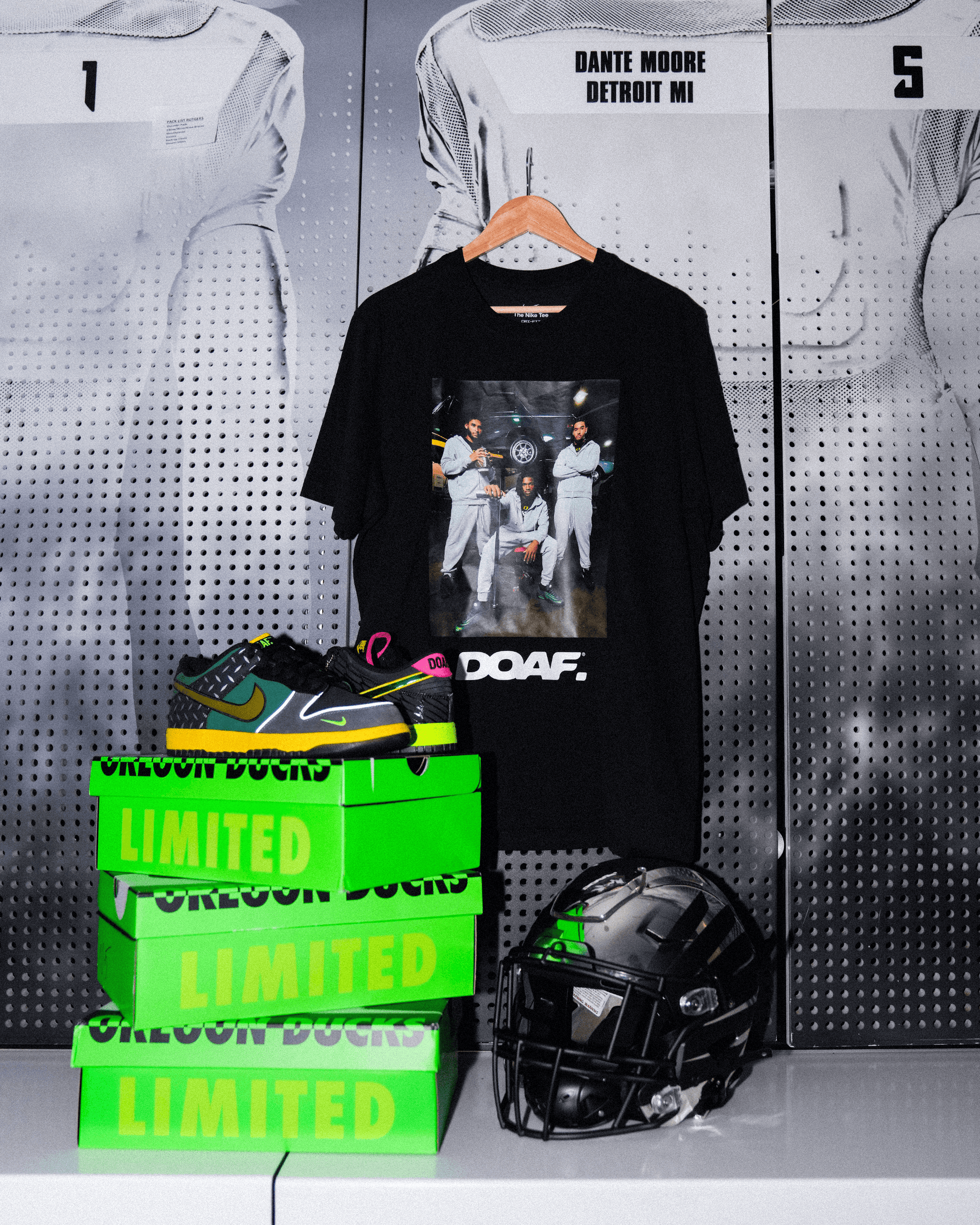 DOAF Tee featuring Dante Moore, Dakorien Moore, and Matayo Uiagalelei hanging up on Dante's locker. There is a football helmet and sneakers stacked on DOAF shoe boxes.
