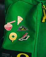 Green Oregon backpack with various colorful DOAF enamel pins on a dark background