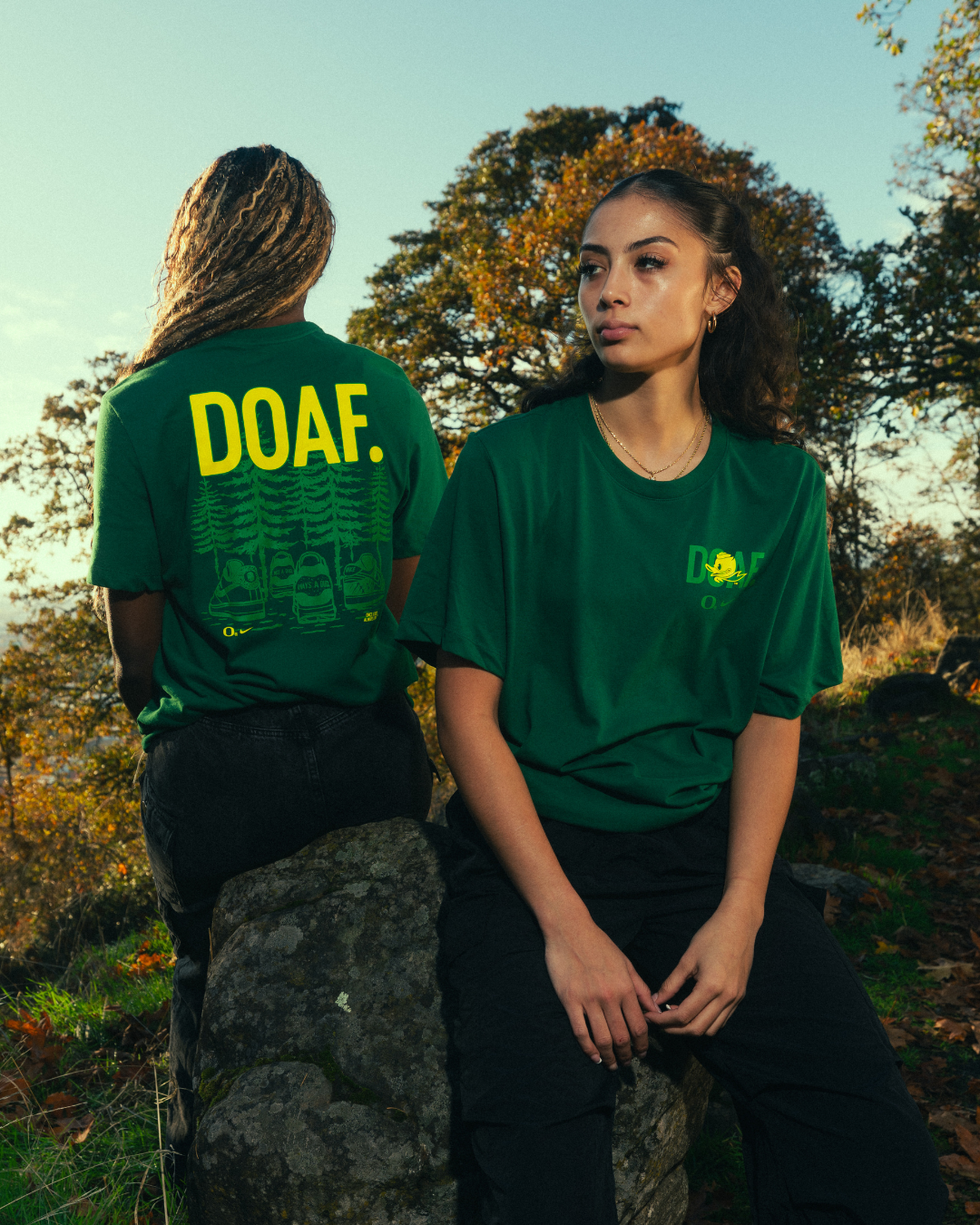 Katie Fiso and Amina Muhammad wearing green t-shirts with 'DOAF' text in a natural setting.