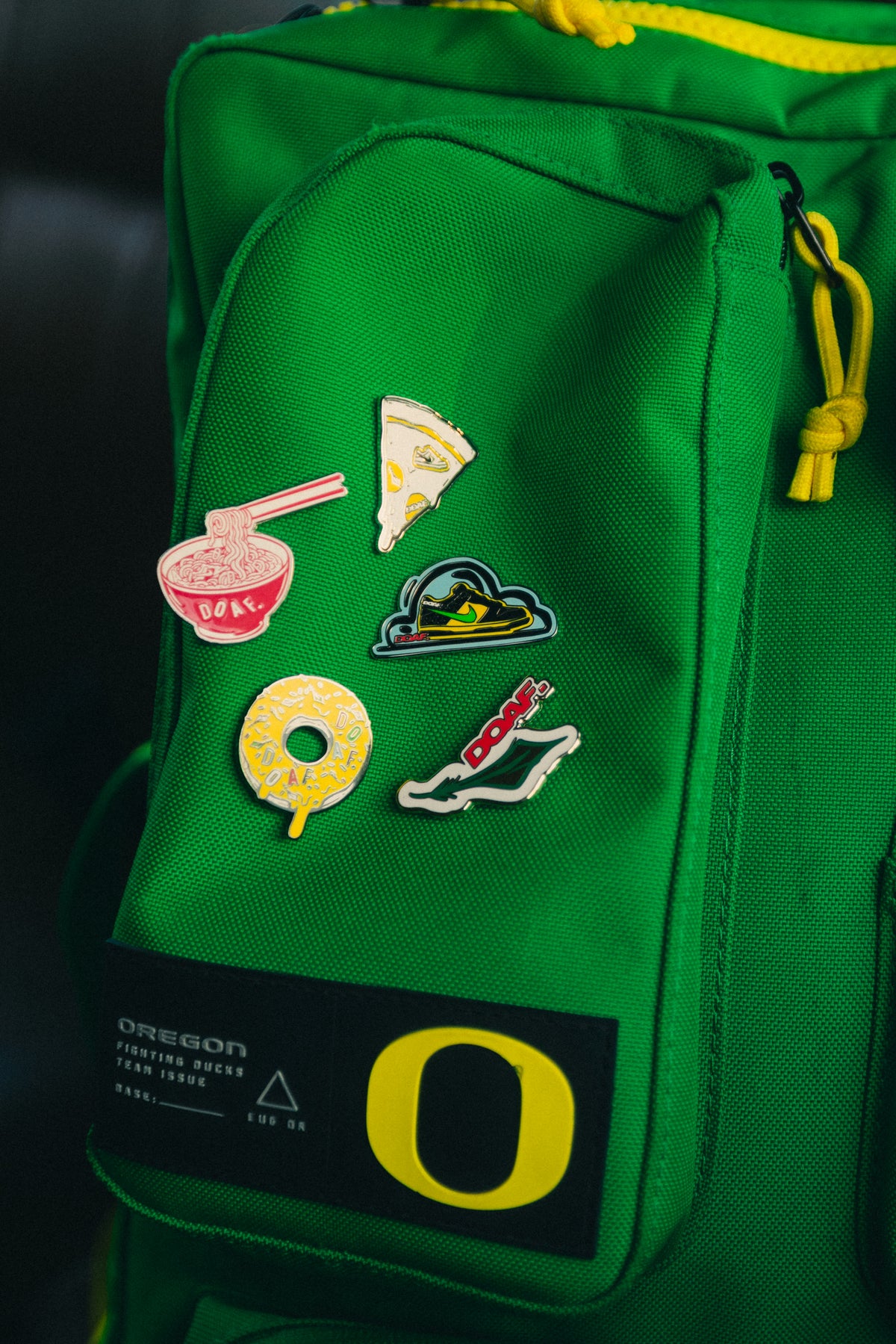Green backpack with DOAF enamel pins on a dark background