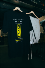 Black DOAF Speedway t-shirt with yellow logo on a hanger in a dark setting.