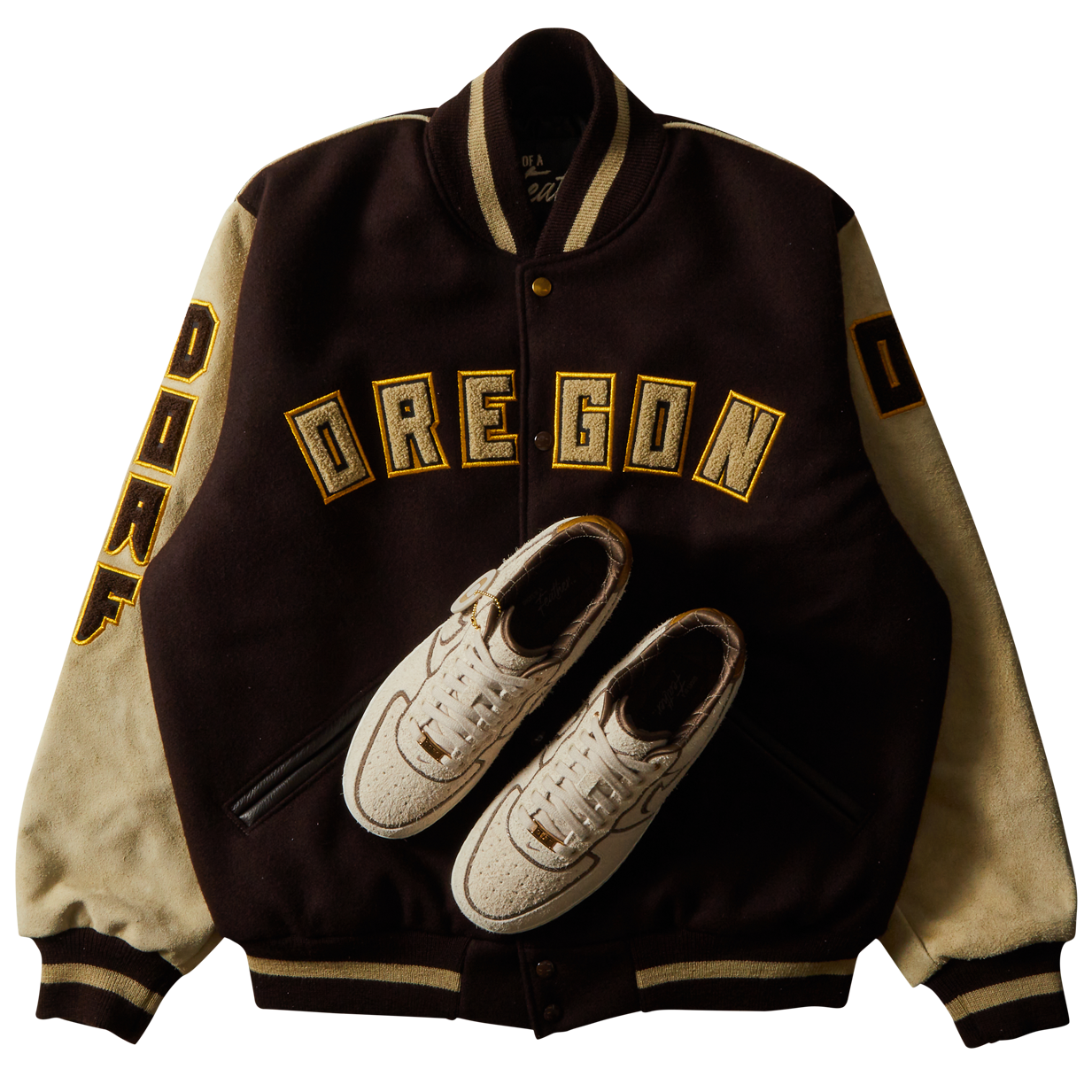 DOAF Varsity jacket with 'OREGON' text and shoe design on a white background. The sneakers reimagine the AF1 ’07 in a sophisticated combination of color and texture that manages to be both luxe and low-key at the same time. An ultra-premium high-texture suede upper in a creamy natural color.
The DOAF Varsity Jacket features a strong “OREGON” read across the chest and "DOAF" on the right sleeve. On the upper back, a metallic gold patch featuring the iconic “O” is stitched onto the jacket.