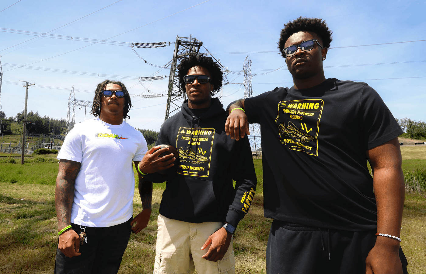 Three athletes standing outdoors with power lines and a clear sky in the background. They are wearing DOAF apparel