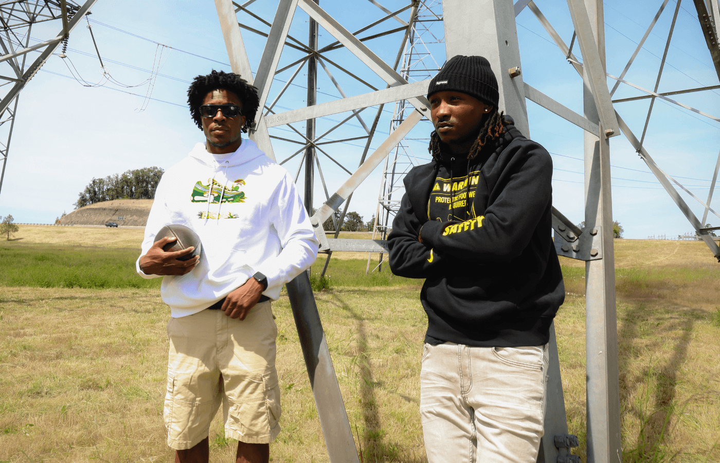 Two athletes standing in front of a large metal structure, possibly a radio tower, with a clear sky background. They are wearing DOAF hoodies.