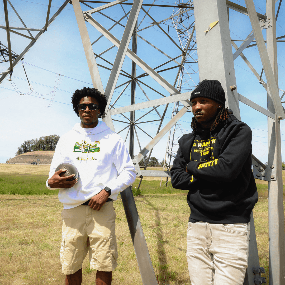 Two people standing in a field with a large metal structure in the background