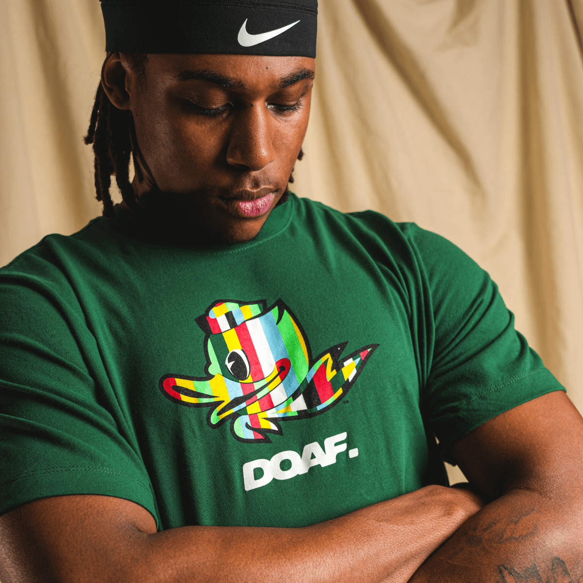 Jamari Johnson wearing a green t-shirt with a colorful Duck graphic and 'DOAF.' text, standing against a beige curtain.