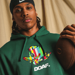 Jamari Johnson wearing a green hoodie with a colorful logo and 'DOAF' text, holding a football.