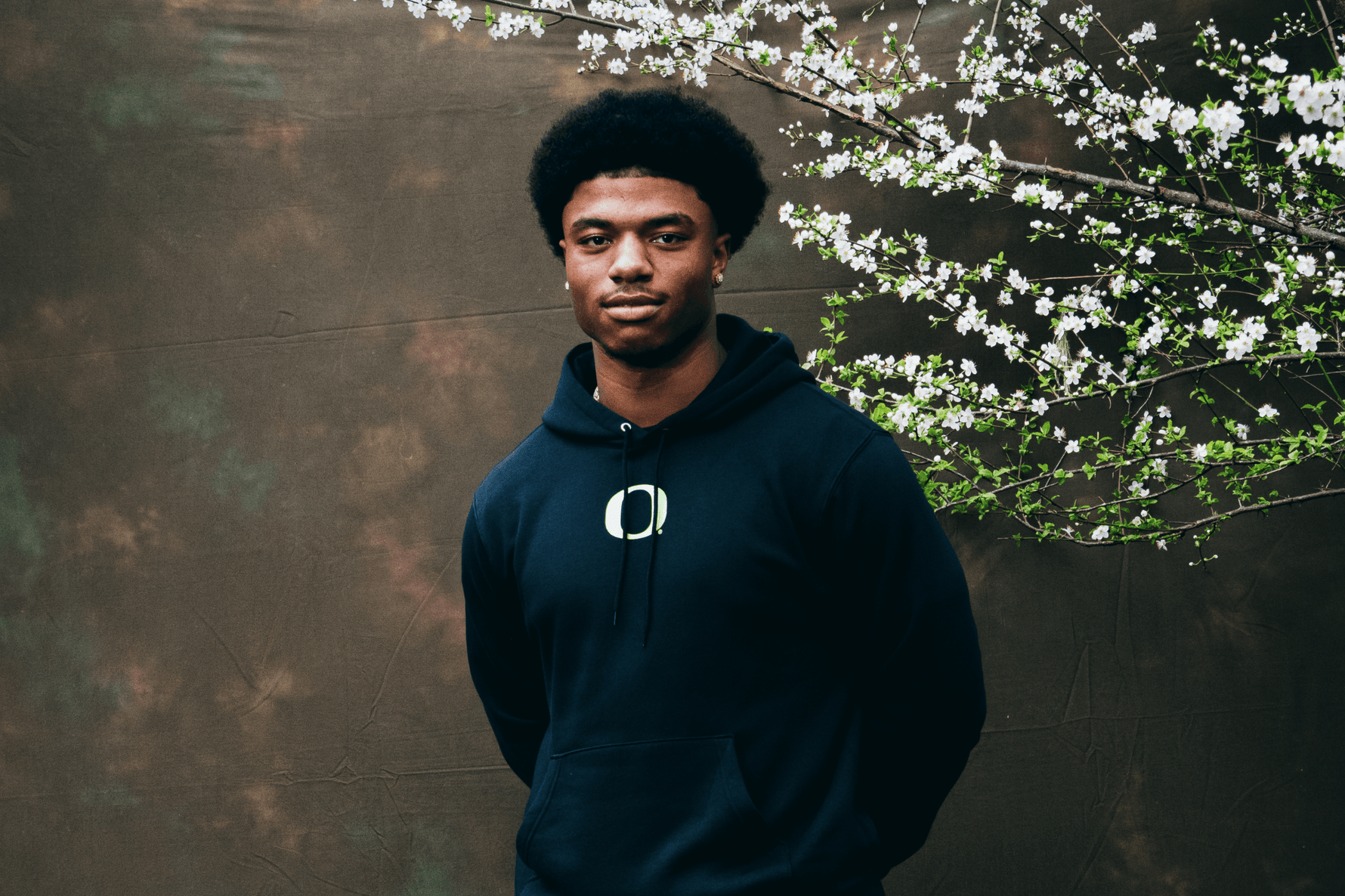 Jerry Mixon wearing a black DOAF hoodie standing against a textured wall with white flowers.