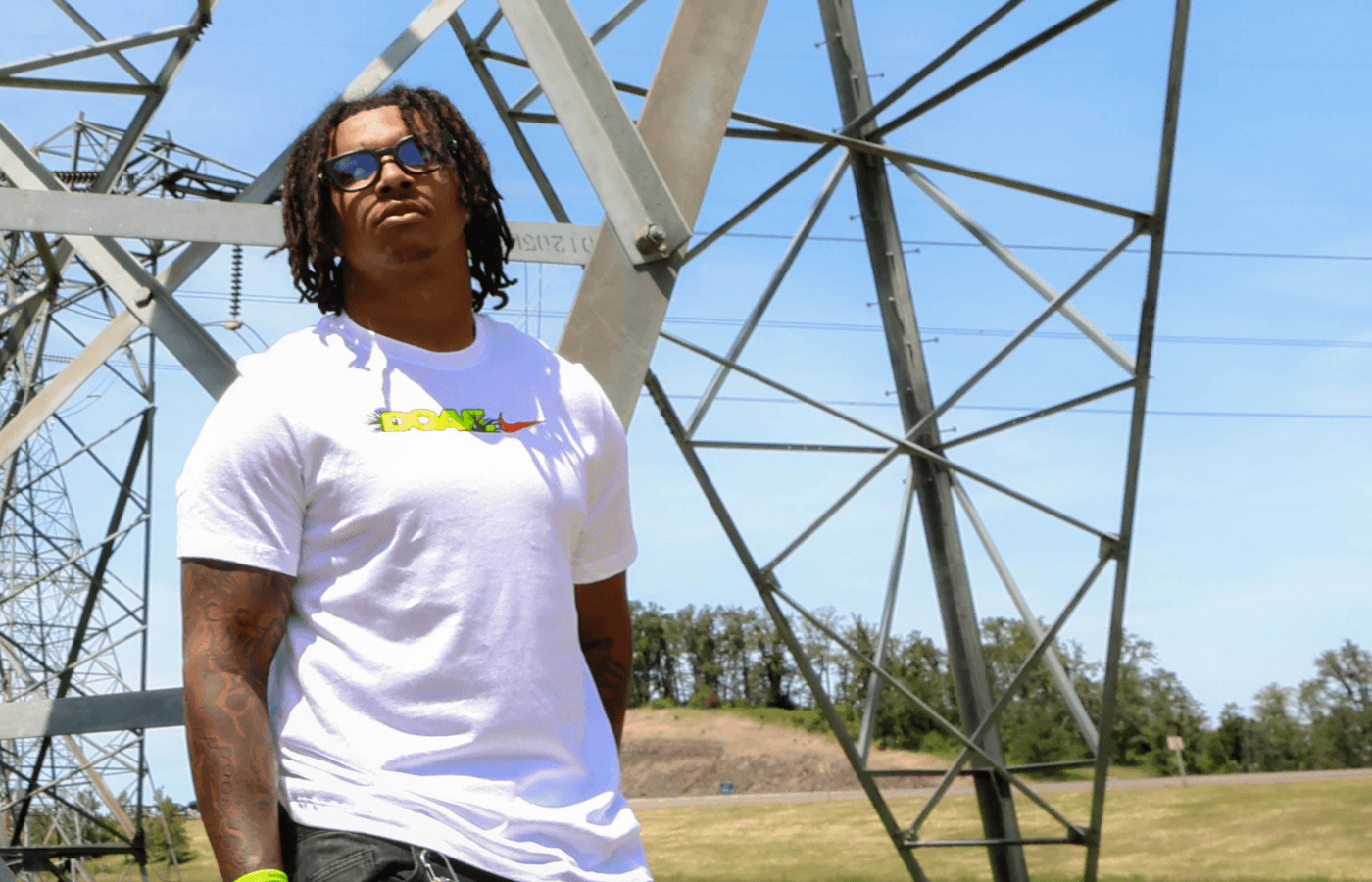 Jordan Davison wearing a white DOAF t-shirt with a colorful design, standing in front of power transmission towers.
