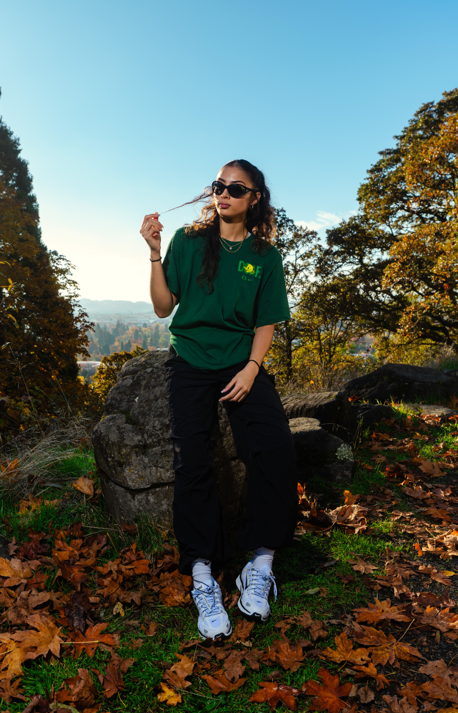 Katie Fiso standing outdoors in a natural setting with trees and rocks. She is wearing a green DOAF tee