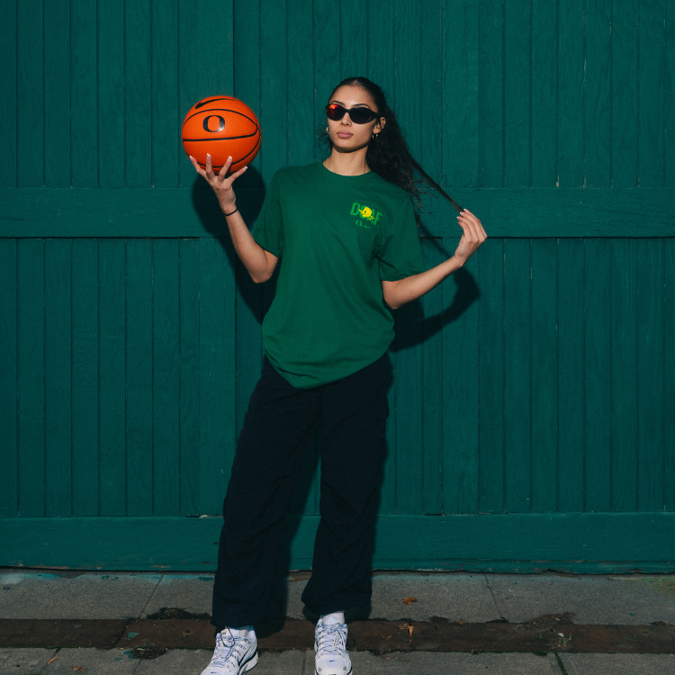 Katie Fiso holding a basketball against a green wall. She is wearing a green DOAF tee