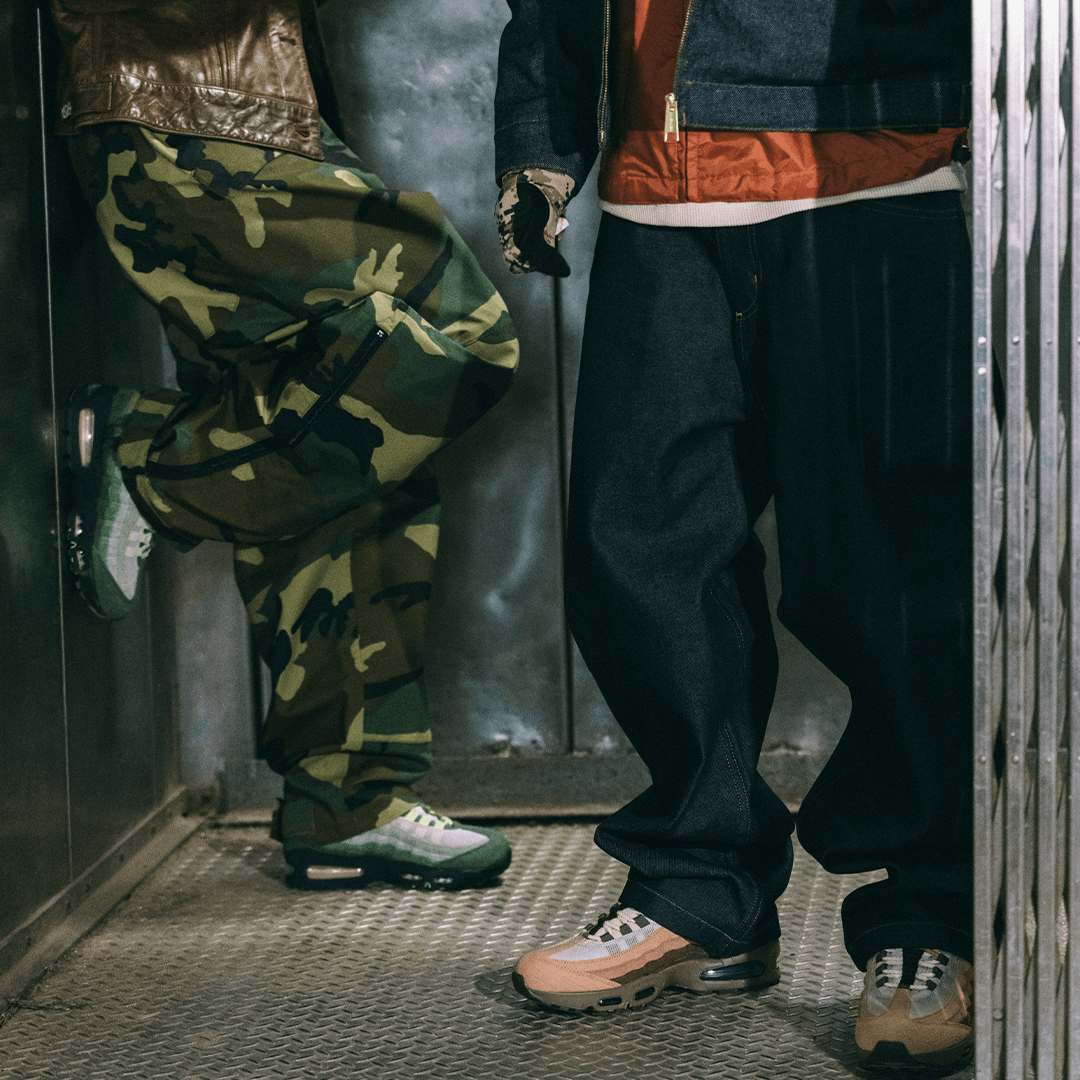 Two people wearing colorful pants and  DOAF sneakers in a dimly lit room.