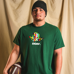 Teitum Tuioti wearing a green DOAF t-shirt with a colorful Duck graphic and text, holding a football against a beige curtain background.