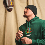 Teitum Tuioti wearing a green hoodie with a colorful logo and 'DOAF' text, holding a football against a beige curtain background.