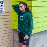 Katie Fiso wearing a set of DOAF gear, including black world wide webbed shorts,  against a green wall.